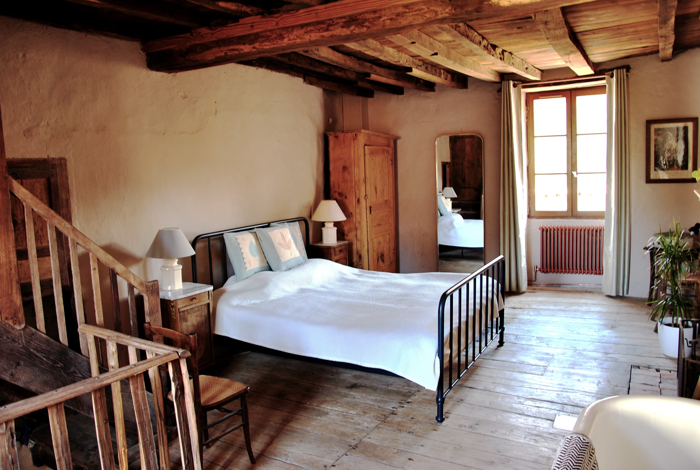 Rustic bedroom with a black metal bed, exposed wooden beams, and wide plank floors.