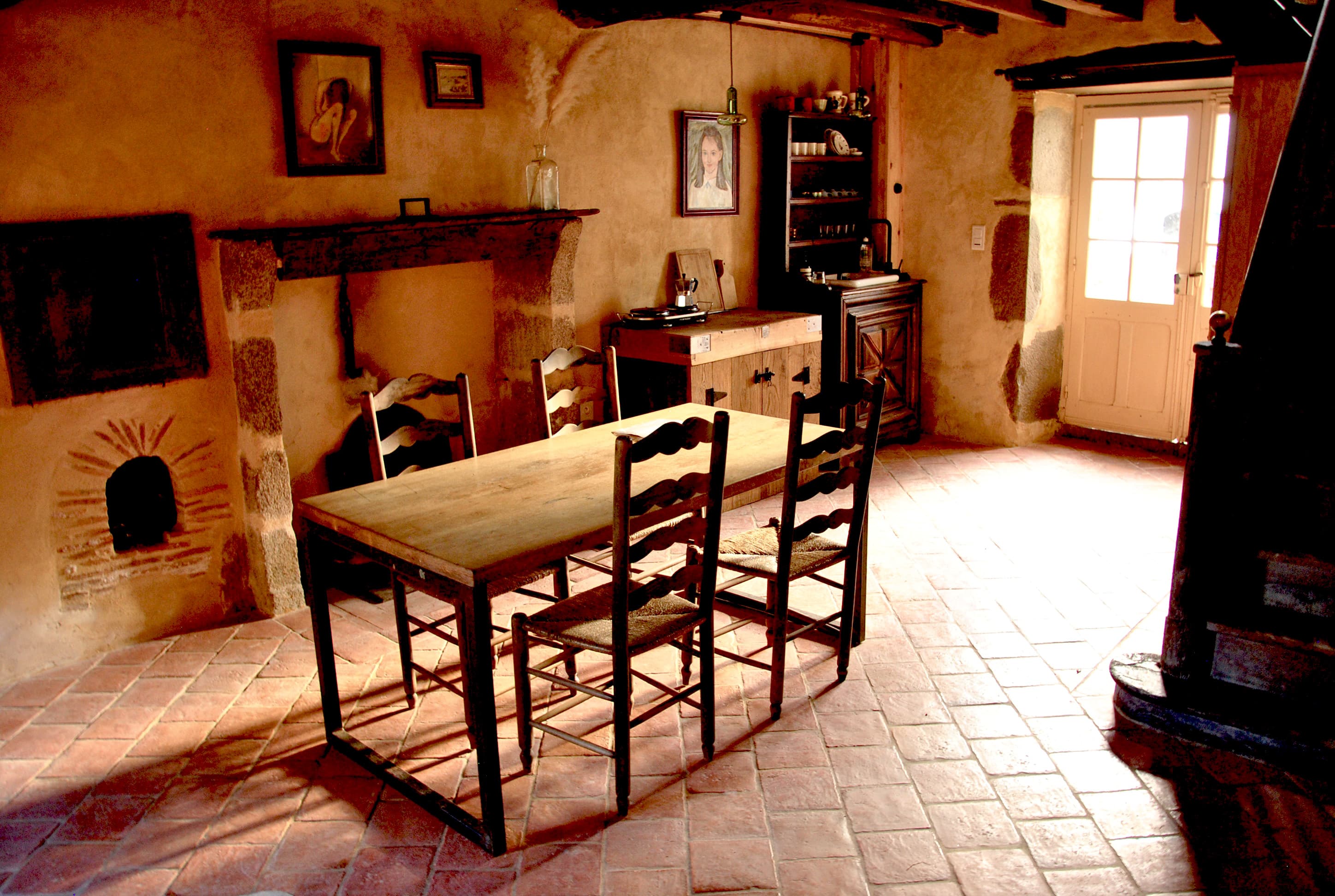 Rustic dining area with a wooden table, ladder-back chairs, and warm terracotta tile floors.