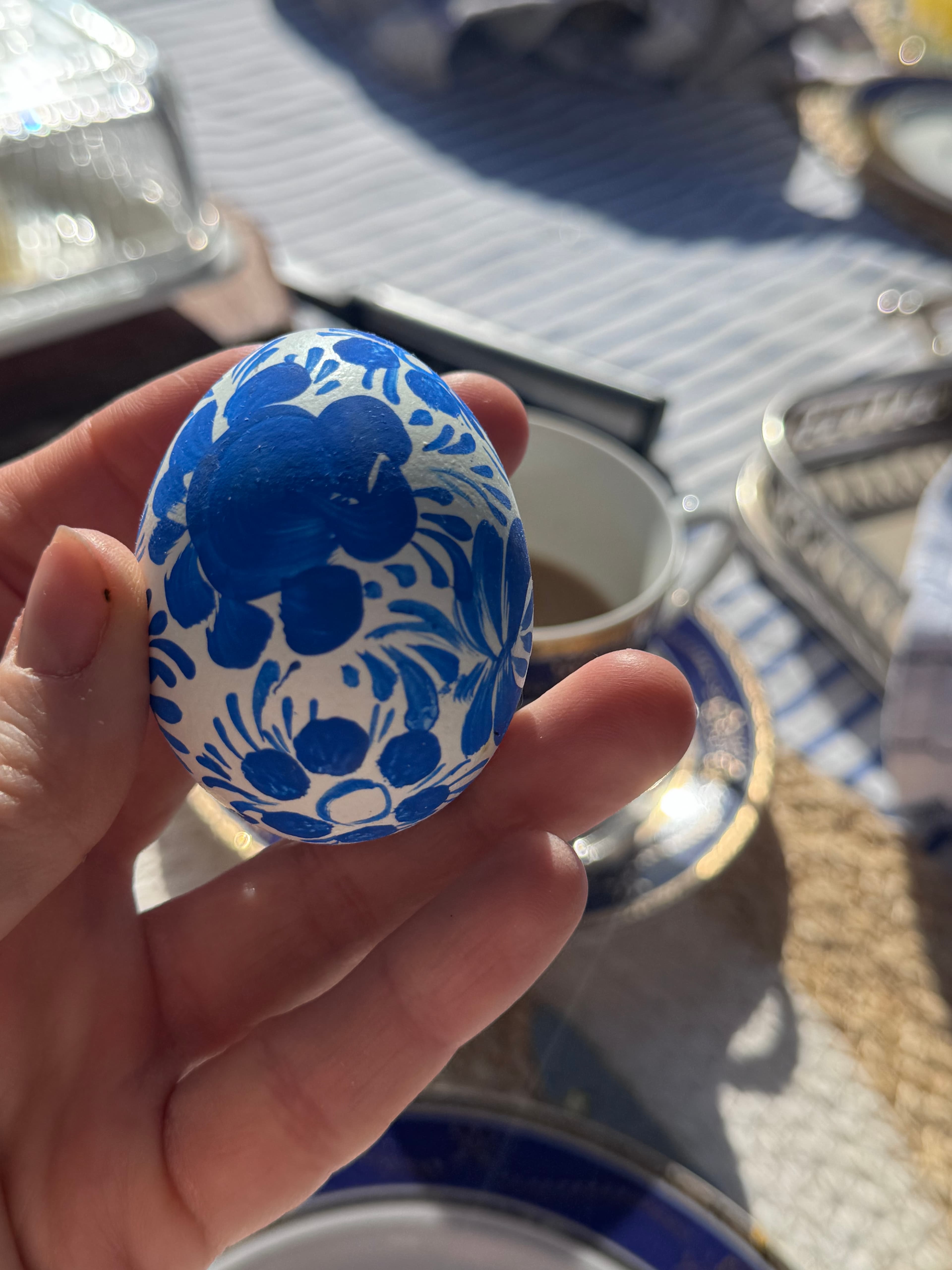A hand holds a white egg decorated with intricate blue floral patterns in Gzhel style.