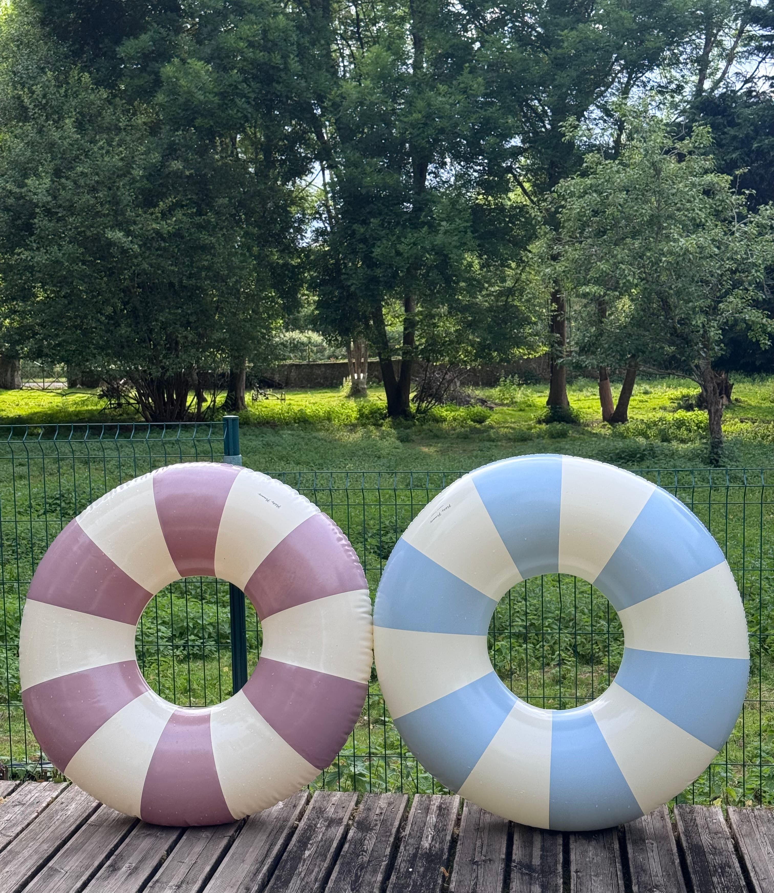 Purple and blue striped inflatable swim rings stand on a wooden deck outdoors.