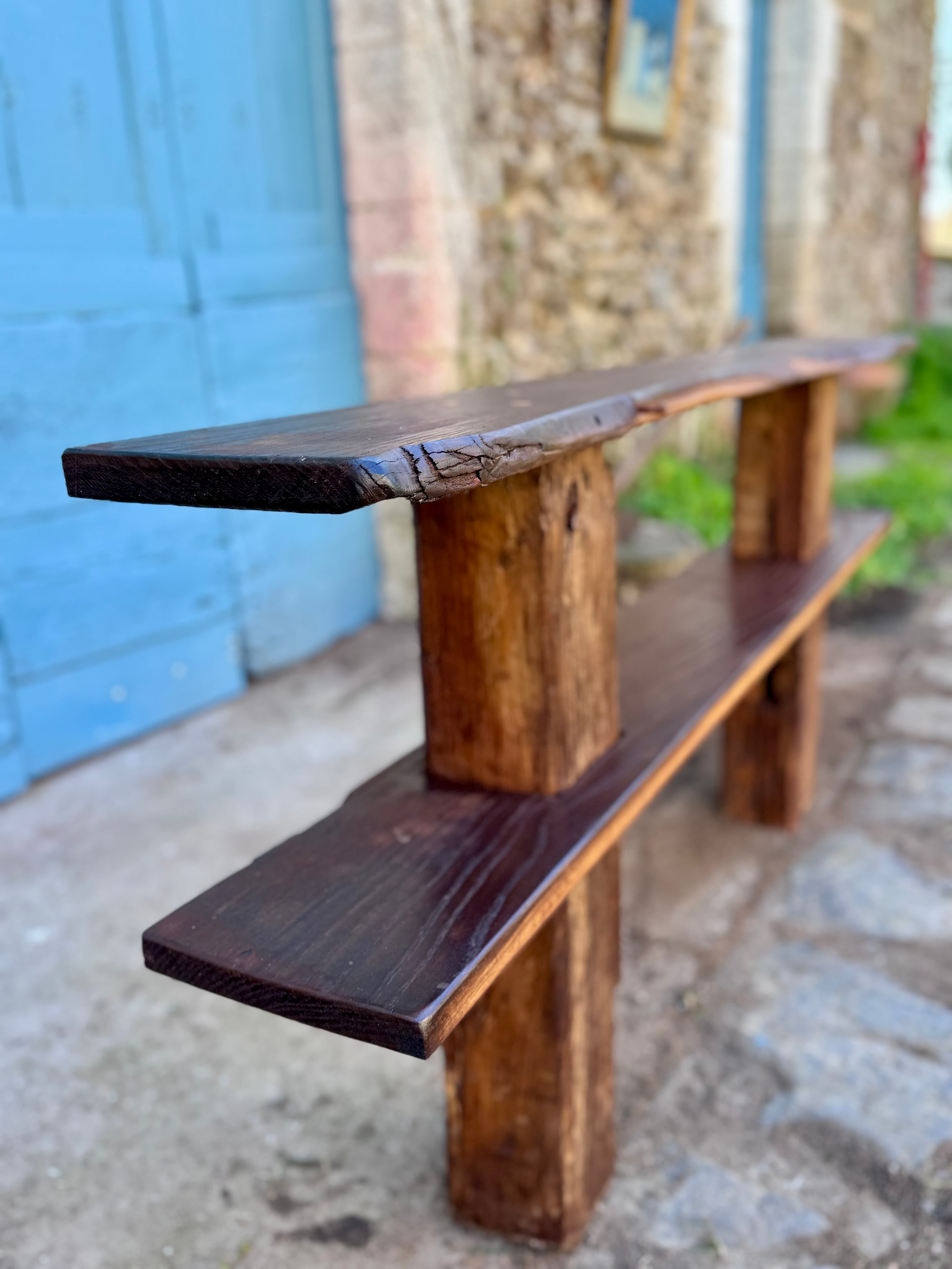 Rustic dark wood bench with two shelves and live edges outside a blue door.